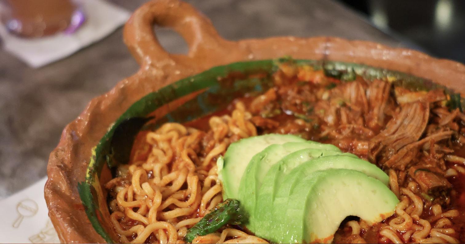 Birria ramen in a clay bowl topped with avocado