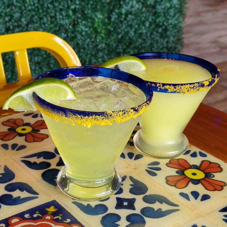 Two classic lime margaritas with salted rims on a tiled table