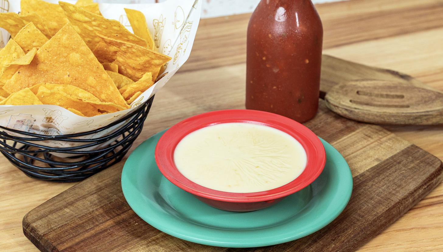 A small bowl of warm white queso with a basket of chips and house salsa