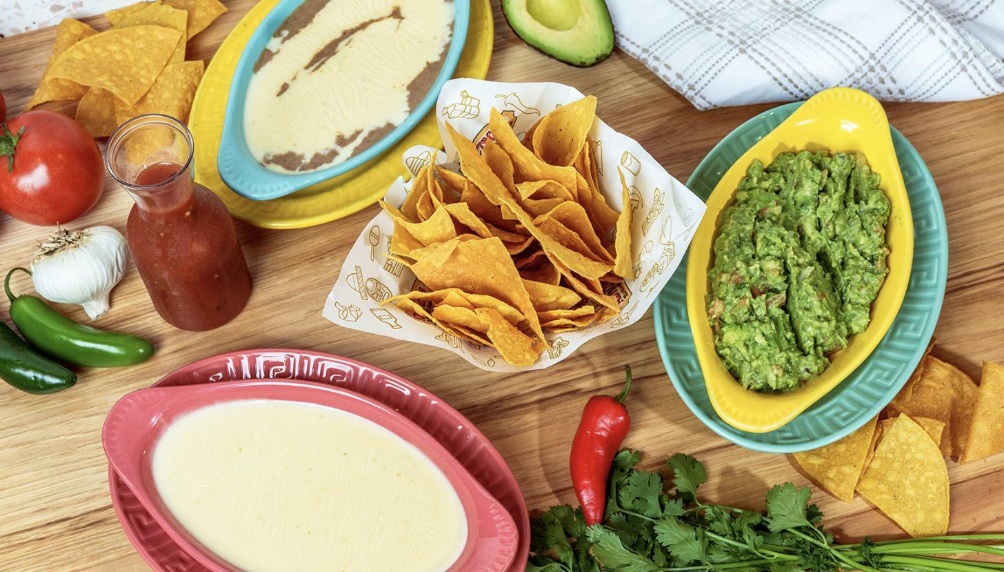 A spread of cheese dip, guacamole, salsa and chips on a wooden table